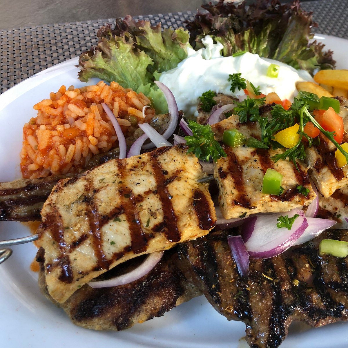 Üppige griechische Grillplatte mit gegrilltem Fleisch, Reis, Zaziki und frischem Salat